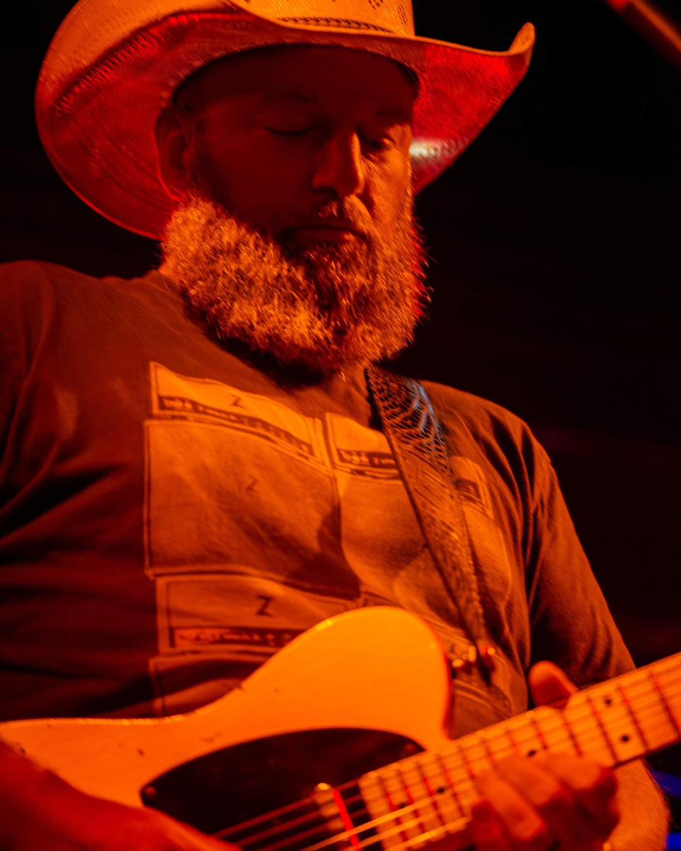 A man with a beard and hat playing guitar