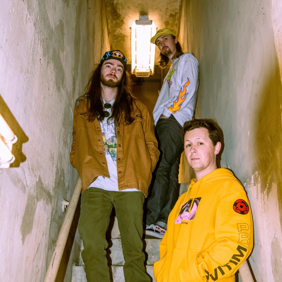 Three people standing in a hallway with one of them wearing a yellow jacket.