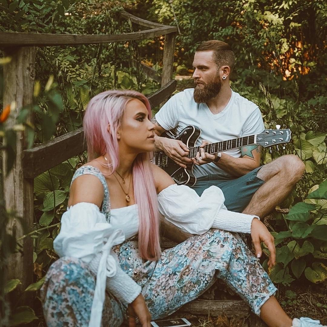 A man and woman sitting on the ground playing guitar.