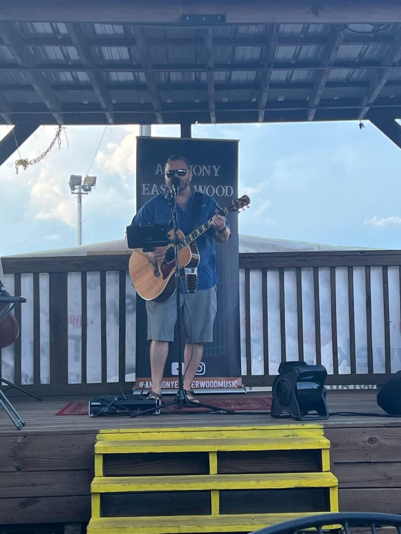 A man playing guitar on stage at an outdoor event.