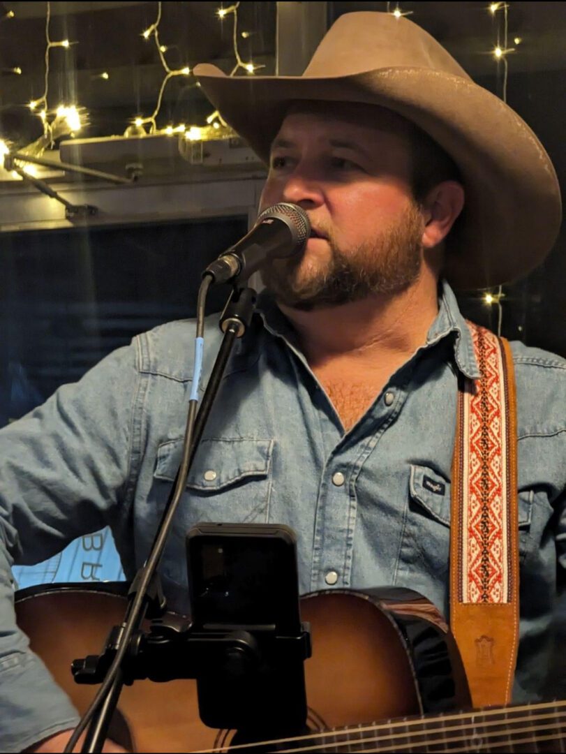 A man in cowboy hat holding a microphone and singing.