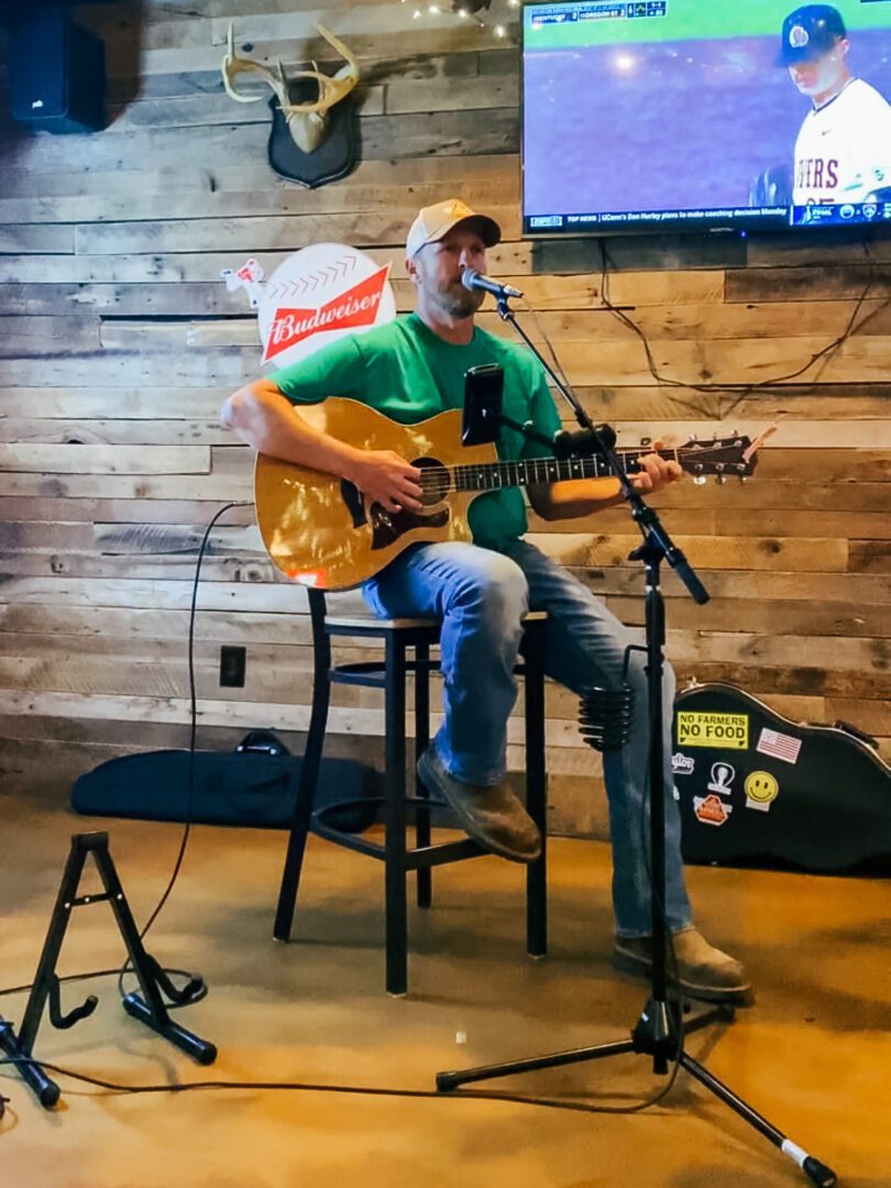 A man sitting on top of a chair playing an acoustic guitar.